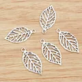 Five silver hollow leaf pendants for DIY jewelry making on a light wooden background - Antique Silver