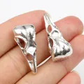 Pair of antique silver bird skull pendants in hand showing size and realistic bone texture - Antique Silver
