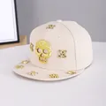 Close-up of golden skull ornaments and rhinestones on a beige flat brim baseball cap - Adjustable / Skull-Beige