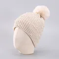 Close-up of beige knit beanie featuring faux pearls, rhinestones and a large fluffy pom-pom - One Size / Beige