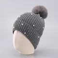 Detail der grauen Strickmütze mit Bommel, eleganten Perlen und glänzenden Kristallen - Einheitsgröße / Grau