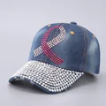 Detailed view of dark blue denim baseball cap featuring pink rhinestone ribbon design - Blue