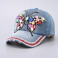 Close-up of denim baseball cap featuring colorful gemstone butterfly and silver studs - Red Rhinestone Brim / Light Blue Butterfly