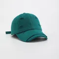 Detailed macro view of distressed holes and frayed edges on green vintage baseball cap - Green