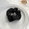 Dettaglio macro dello scrunchie nero in tessuto plissettato con bordi a balze su piatto - Nero