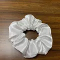 Detailaufnahme eines weißen LED-Haargummis aus Satin auf dunklem Holzhintergrund - Weiß