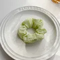 Dettaglio di uno scrunchie verde chiaro in tessuto testurizzato su vassoio di ceramica - Verde