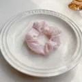 Dettaglio di un elastico per capelli rosa chiaro su vassoio bianco con pieghe morbide - Rosa Chiaro