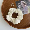 Nahaufnahme eines cremefarbenen Satin-Scrunchies auf einem Holztablett mit Karten - Gebrochenes Weiß