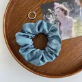 Detail eines graublauen Satin-Scrunchie mit Silberringen auf einem Holztablett - Blaugrün