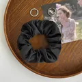 Klassisches schwarzes Satin-Scrunchie mit glatter Seidentextur auf einem Holztablett - Schwarz
