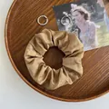 Champagnerfarbenes Satin-Haargummi mit zwei Silberringen auf einem Holztablett - Dunkelgelb