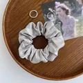 Satin Haargummi in Hellgrau mit minimalistischen Silberringen auf einem Holztablett - Grau