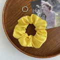 Glänzender hellgelber Satin-Haargummi auf einem Holztablett mit Accessoires - Eigelbgelb