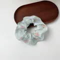 Detailed view of light blue floral organza scrunchie with embroidery on a wooden tray - Rose Embroidered Blue