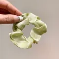 Pale green organza scrunchie with pearlescent texture held by hand in a close-up view - Green