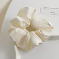 Détail d'un chouchou en satin blanc crème posé sur un plateau texturé décoratif - Blanc Cassé