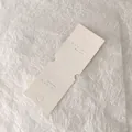 Detail of off-white paper jewelry display card with logo and hanging holes - Square Style (U Y U · U Y U) / Off White