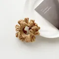 Close-up of beige plush faux fur hair scrunchie with soft fleece texture on white plate - Brown
