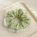Détail d'un chouchou à carreaux verts avec bordure en dentelle blanche sur plateau - Carreaux Verts