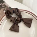 Elegante coletero de satén marrón oscuro con cintas largas sobre un plato de cerámica - Café Oscuro