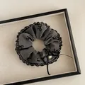 Detail von dunkelgrauem Scrunchie mit Spitzenkante, Schleifenstickerei und Anhänger - Spitze Schleife Grau Haargummi Stil