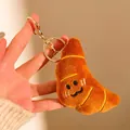Gros plan d'un porte-clés croissant en peluche avec visage brodé dans la main - Croissant (Porte-clés)