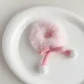 Detail eines rosa Plüsch-Haargummis mit Strickschleife und weißen Bommeln auf Teller - Rosa