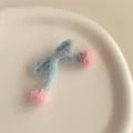 Détail d'une barrette nœud en tricot bleu clair avec des pompons roses sur un plateau - Bleu Ciel