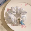 Close-up of white scrunchie with blue bows, lace trim and handmade tag on a ceramic tray - White with Blue Bow Pattern and Bow Accessory