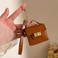 Dettaglio di un mini portachiavi a borsa in pelle marrone con cuciture fini dorate - Cioccolato