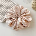 Macro detail of champagne satin scrunchie with soft pleated texture and silk gloss - Apricot