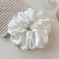 Detail of an oversized white satin scrunchie with a soft pearlescent sheen and pleated texture - White