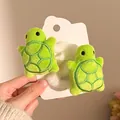 Close-up of two cute green plush turtle hair scrunchies on a heart-shaped display card - Green