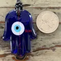 Detailed view of a 5cm blue glass Evil Eye Hamsa pendant with a black braided cord - Hamsa Hand