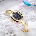 Detalle de reloj ovalado dorado con esfera negra y agujas azules sobre cristal - Esfera Negra Caja Dorada