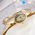 Detalle de reloj brazalete dorado ovalado con números romanos sobre bandeja de cerámica - Esfera Dorada Caja Dorada