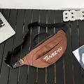 Bolso bandolera de lona marrón con letras blancas y parches en una mesa negra - Marrón