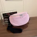 Light pink nylon crossbody saddle bag with adjustable black strap on wooden surface - Pink