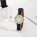 Detail of round gold quartz watch with tri-color nylon strap on a white sandy display - Blue