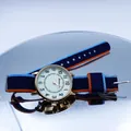 Close-up of golden quartz watch with tri-color striped nylon strap on reflective surface - Blue