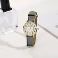 Detail of a gold case watch with a tricolor nylon strap next to a perfume bottle - Gray