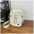 Détail d'un sac bandoulière en nylon beige avec poche à cordon sur une table en bois - Blanc Cassé