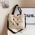 Beige canvas tote bag with brown straps and fashion text on a minimalist table - White