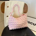 Pink pleated crossbody bag with golden hardware and bubble fabric texture on leather chair - Pink
