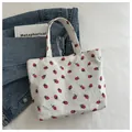 Close-up of white corduroy tote bag featuring vibrant red strawberry patterns on denim - White