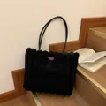 Furry black plush tote bag with purple logo patch and leather handles displayed on stairs - Black