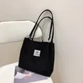 Minimalist black corduroy tote bag with dual shoulder straps and a white square logo patch - Black