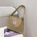 Minimalist beige corduroy tote bag with dual handles and fabric patch on a chair - Khaki
