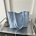 Light blue canvas tote bag with front pocket and fashion label on a metal cart - Blue